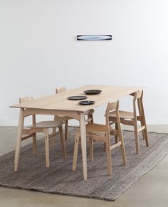 a wooden table with four chairs around it on a rug in front of a white wall