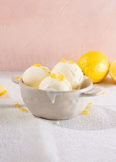 three scoops of ice cream in a bowl with lemons around it on a table