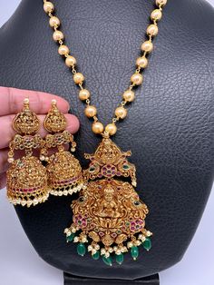 Goddess Lakshmi Nakshi Red Green Stone Color Beads Pendent Set with matching Jhumki, comes with complementary pearl malaColor : Golden MatteSize : Mala Length : Approx 18 Inches; Pendent Length : Approx 4 Inches; Earring Length : Approx 2.25 Inches;Stones : CZ Red Green Stone --Color-- Beads Pearls Temple Jewelry Sets With Dangling Beads For Celebrations, Traditional Jewelry Sets With Dangling Beads For Celebration, Temple Jewelry With Dangling Beads For Diwali, Temple Jewelry Sets With Dangling Beads For Wedding, Diwali Temple Jewelry With Dangling Beads, Traditional Pearl Necklace With Dangling Beads For Weddings, Temple Jewelry Mala With Latkans For Celebrations, Festive Temple Jewelry Sets With Round Beads, Festive Jewelry Sets With Dangling Beads For Festivals