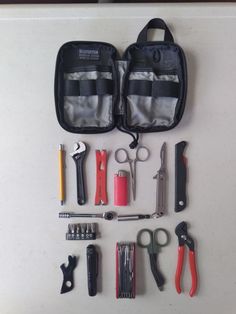 the contents of a tool bag are laid out on top of a white table with scissors, pliers and other tools