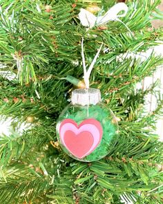 a glass ornament with a heart on it is hanging from a christmas tree