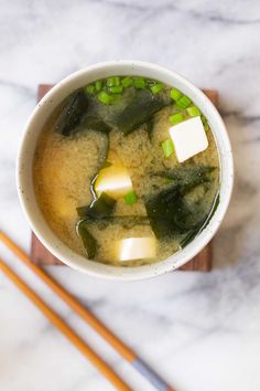 a white bowl filled with soup next to chopsticks on a marble counter top