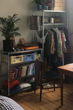 a room with a metal shelf filled with books and plants next to a bed covered in blankets