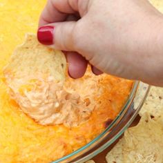 a person is dipping tortilla chips into a bowl full of dip and cheese