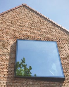 a brick building with a large mirror on it's wall and trees reflected in the window