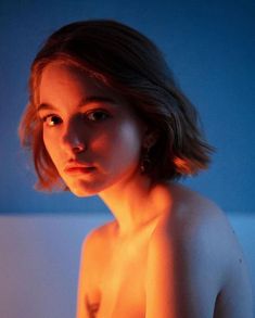 a naked woman with no shirt on in front of a blue wall, looking at the camera