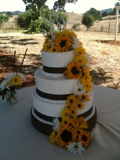 a three tiered cake with sunflowers and ribbons on the top is sitting on a table