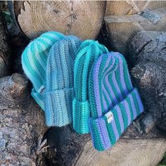 two knitted hats are sitting on top of logs in the woods, one blue and one green