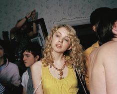 a group of people standing around each other in a room with one woman wearing a yellow dress