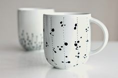 two white coffee mugs sitting on top of a table next to each other with black dots