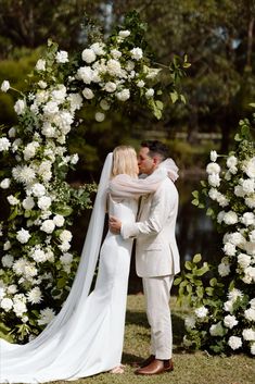 a bride and groom kissing under an arch of flowers