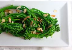 a white plate topped with broccoli and almonds on top of a table