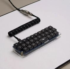 a computer keyboard sitting on top of a white table next to a black and silver cord