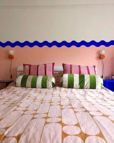 a bed with colorful pillows on it in a pink and white room, next to a blue nightstand