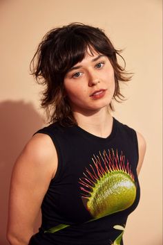 a woman wearing a black shirt with a green flower on it's chest and her hair blowing in the wind