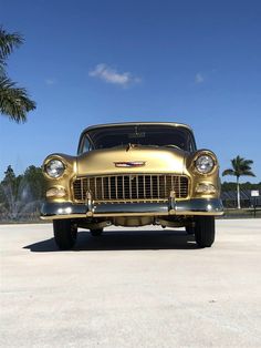 an old gold car is parked in the parking lot with palm trees and blue sky behind it