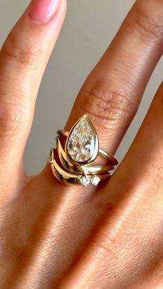 a woman's hand wearing a gold ring with a pear shaped diamond on it