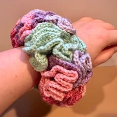 a woman's hand is holding a multicolored crocheted knitted bracelet