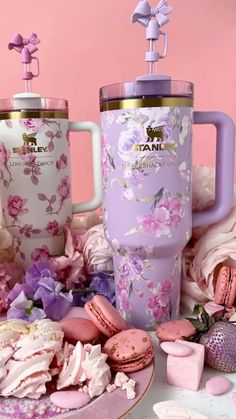 two pink and white mugs sitting on top of a table next to macaroons