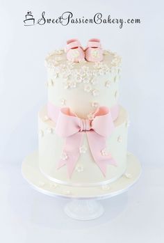 a three tiered cake with pink bows and flowers on the top is decorated in white frosting