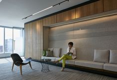 a woman is sitting on a couch in an office with wood paneling and floor to ceiling windows