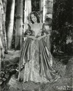 an old black and white photo of a woman in a dress standing by some trees