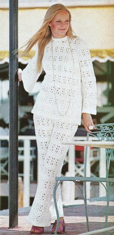 a woman is standing next to a table and chair wearing a white crochet suit