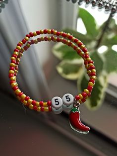 a red and yellow beaded bracelet with two numbers on it next to a potted plant