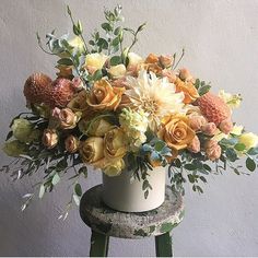 a white vase filled with lots of flowers on top of a wooden stool next to a wall