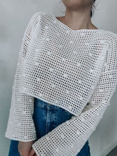 a woman wearing a white knitted sweater with openwork on the sleeves and shoulders