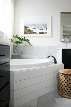 a bathroom with a large white bathtub next to a wooden stool and black cabinets