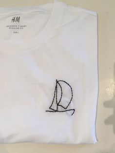 a white t - shirt with a sailboat embroidered on it