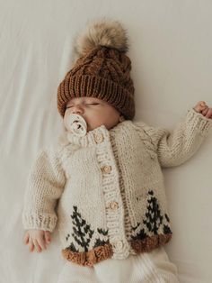 a baby is wearing a knitted sweater and hat while laying on a white sheet