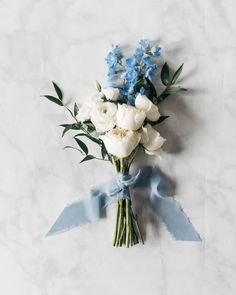 a bouquet of white and blue flowers on a marble surface with a light blue ribbon