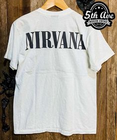 a white shirt with the word nirvana on it hanging from a hanger against a wooden wall