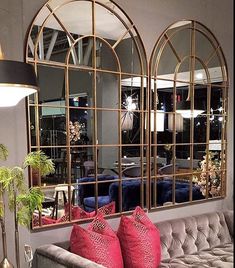 a living room filled with furniture and large mirrors on the wall above it's windows