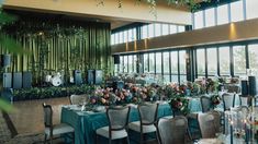 a room with tables and chairs covered in blue cloths, flowers and greenery