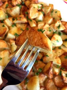 a fork with some food on it in front of a pile of potatoes and parsley