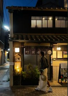 a man is walking down the street in front of a building at night with lights on