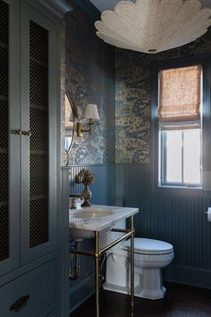 a white toilet sitting next to a sink in a bathroom under a window with blue walls