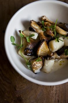 a white bowl filled with cooked mushrooms and garnished with green leaves on top