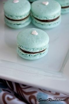 there are four blue macaroons on the plate and one is green with white hearts