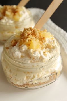 two small jars filled with whipped cream and pineapple toppings on top of a white plate