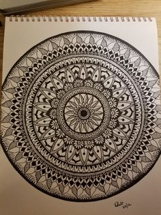 a spiral notebook with an intricate design on the cover, and a pen next to it