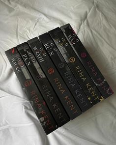 a stack of five books sitting on top of a white bed covered in sheets and pillows