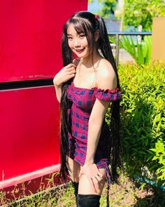 a woman with long black hair standing in front of a red wall and smiling at the camera