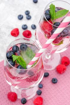 two glasses filled with fruit and ice on top of a pink table cloth next to strawberries