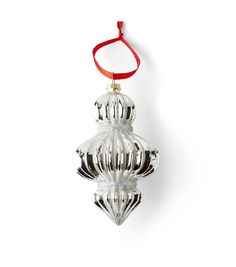 a silver ornament hanging from a red ribbon on a white wall with an orange cord