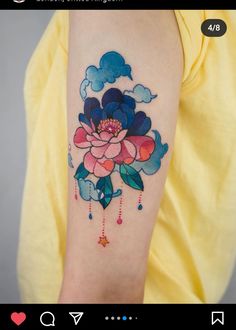 a woman's arm with flowers and clouds tattooed on the back of her arm