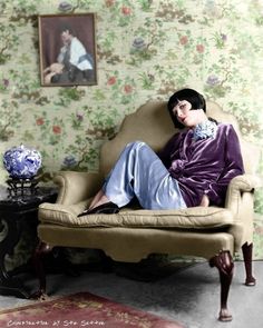 a woman sitting on top of a chair in front of a wallpapered room